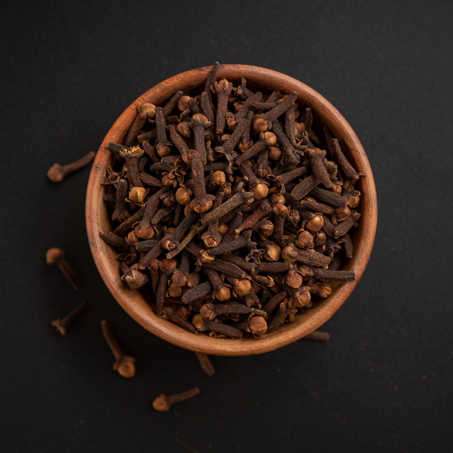 Premium quality whole clove buds in a wooden bowl on black background