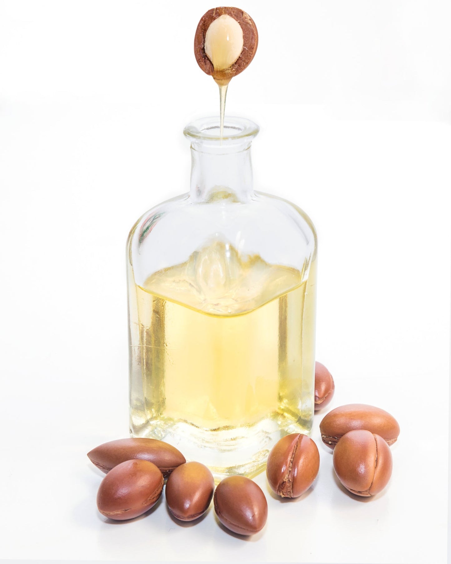 Pure cold-pressed argan oil in a glass bottle with argan nuts on a white background