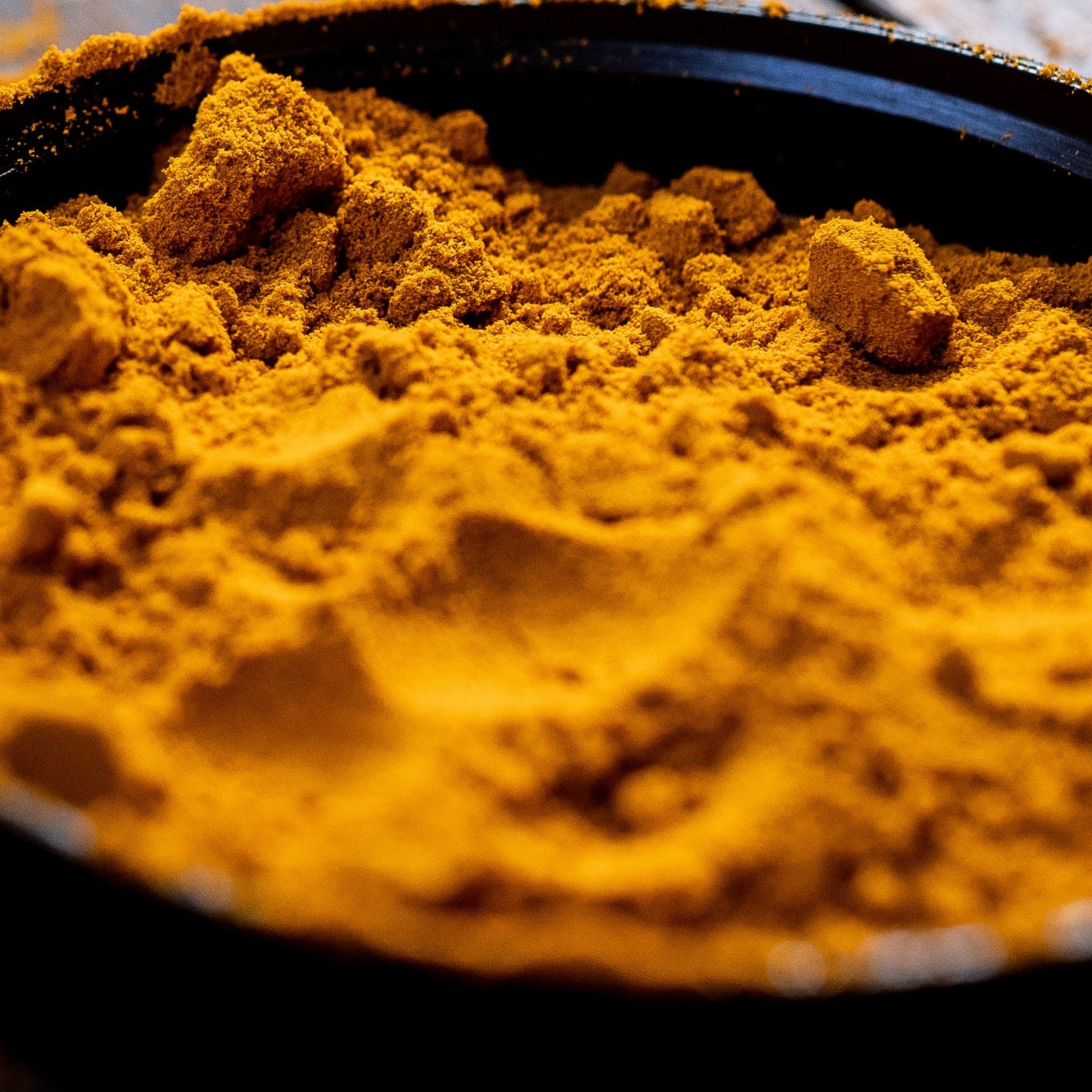 Close-up of golden spice blend powder with turmeric and herbs in black container
