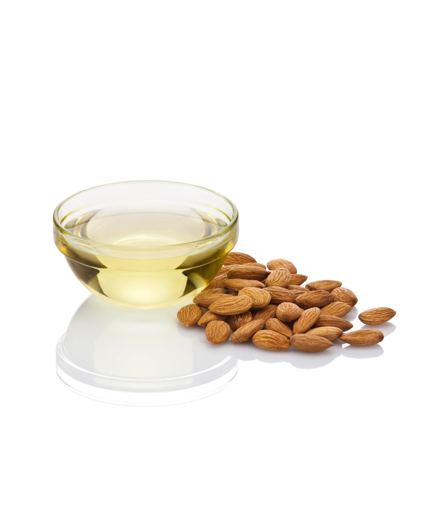 Glass bowl of cold-pressed sweet almond oil with raw almonds on white surface
